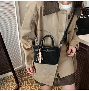 Detail of a black square bucket bag with wooden beads and strap on a beige trench coat