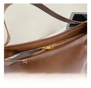 Détails de la fermeture éclair dorée et du gland tressé sur le sac en cuir brun