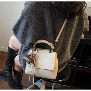 Macro detail of beige lychee grain leather crossbody bag with brown heart charm