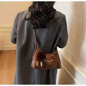 Detail of dark brown leather handbag with gold crescent buckle and fuzzy bag charm