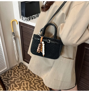 Detail of black checkered handbag with unique colorful beaded charm and sleek strap