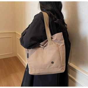 Détail latéral d'un sac cabas en toile beige montrant le tissu et l'étiquette de marque