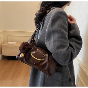 Detail of dark brown hobo bag featuring a gold crescent buckle and a fuzzy fur charm