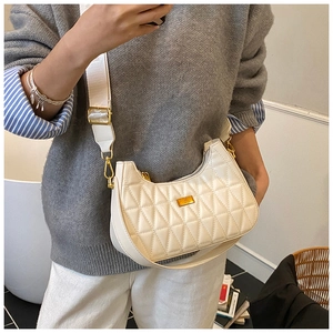 Detailed shot of white quilted saddle bag with wide strap and gold hardware on a model