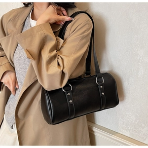 Close-up of black leather bowling bag with silver metal rings on a beige trench coat