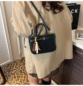Detail of black woven shoulder bag with unique wooden bead tassel and metal buckle