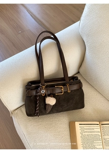 Detail of dark brown suede baguette bag with leather strap and plush charm on a sofa