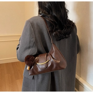 Detail of a dark brown leather baguette bag with a gold crescent buckle and plush pom-pom