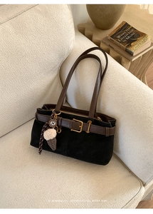 Macro shot of black suede shoulder bag with brown leather strap and gold buckle detail