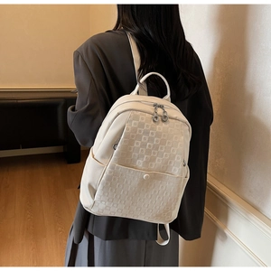 Detail of a beige leather backpack with plaid embossing and metal zippers on a model