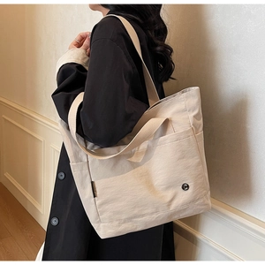 Détail d'un grand sac fourre-tout en toile beige avec poche avant porté sur un manteau noir