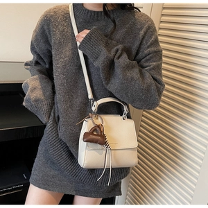 Detailed shot of a beige leather crossbody bag with a mini brown charm on a model