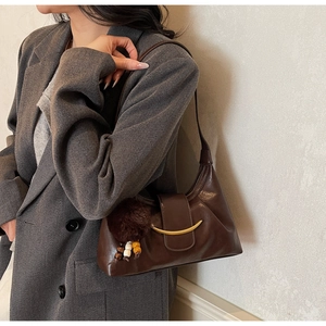 Detail of dark brown leather underarm bag with gold crescent clasp and plush charm