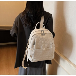 Detail view of a cream faux leather backpack with embossed checkered pattern on a model