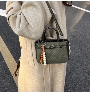Detail of dark green checkered bag with a wooden bead charm on a beige wool coat