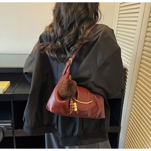 Detailed close-up of dark red shoulder bag with golden crescent buckle and fur charm