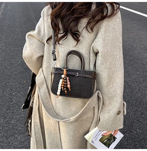 Detail of dark brown checkered crossbody bag with beaded tassel charm on a street