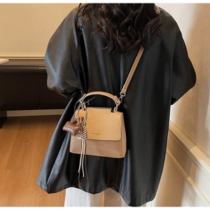 Detail of light brown lychee textured leather square bag with a mini charm and thin strap