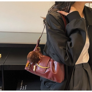 Detail of burgundy underarm bag with gold metal trim and decorative plush pendant