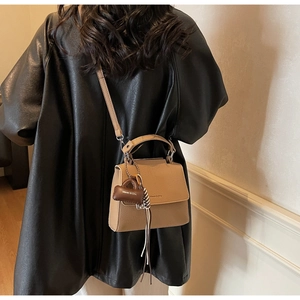 Detail of camel lychee leather shoulder bag with tassels and brand logo on model