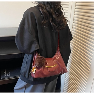Detail of burgundy leather shoulder bag with crescent gold buckle and plush charm