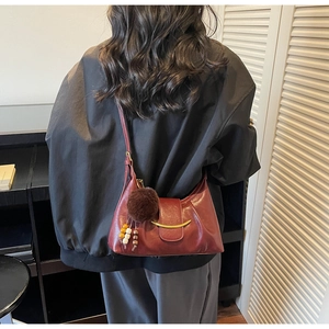 Close-up of wine red crescent shoulder bag featuring gold metal trim and tassel charms