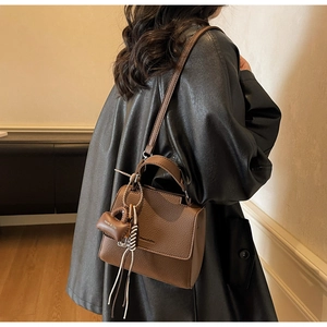 Detail of a brown lychee pattern leather shoulder bag with a Maven & Chic mini charm