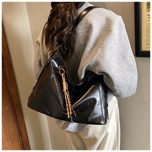 Détail du sac hobo noir brillant avec pendentif en corde tressée et texte mode