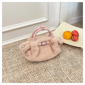 Detalle de bolso de peluche rosa con asa de cuero y hebilla metálica decorativa