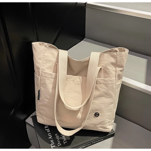 Détail du cabas beige avec doubles anses et logo métallique sur tissu texturé