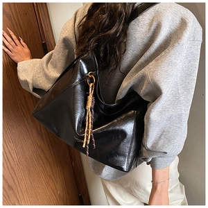 Vue détaillée du sac à bandoulière en cuir brillant noir avec pendentif en corde tressée
