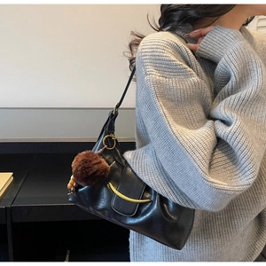 Detail of black leather hobo bag featuring a gold crescent buckle and plush charm on the strap