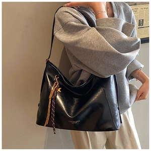 Détail d'un sac cabas en cuir noir brillant avec pompon tressé et inscription mode