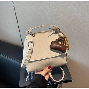 Close-up of cream pebble leather mini bag with brand charm and adjustable strap