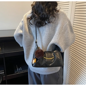 Detail of black underarm bag featuring a gold crescent buckle and plush charm detail