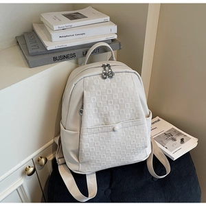 Detail of cream backpack showing checkered embossing, dual zippers, and front flap pocket