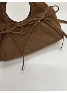 Détail du sac à main en daim marron foncé avec nœuds décoratifs et poignée ronde