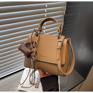 Detail of beige lychee texture leather handbag with branded gold lettering and charm