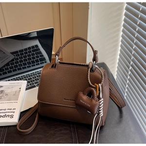 Detailed shot of brown lychee grain leather crossbody bag with logo charm detail