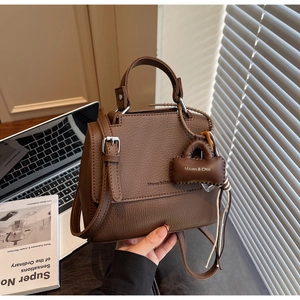 Close-up of brown litchi pattern leather bag with silver metal buckle and Maven & Chic logo