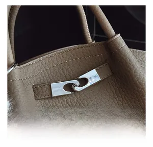 Detail of brown litchi pattern leather bag featuring a silver metal buckle and plush ball