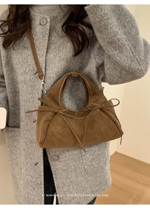 Sac bandoulière en daim marron avec nœuds latéraux porté sur un manteau en laine gris