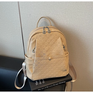Detail of beige faux leather backpack showing square embossed texture and metal zipper pulls