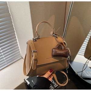 Detail of tan pebble leather bag with silver buckle and mini bag charm accessory