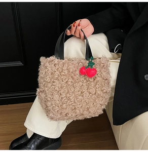 Detail of beige faux fur bucket bag with black handle and red cherry charm accessory