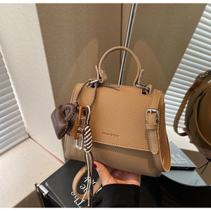 Detail of khaki square handbag with lychee texture and decorative heart charm strap