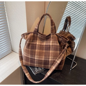 Detailed view of brown plaid woolen tote bag texture with adjustable strap on wood table