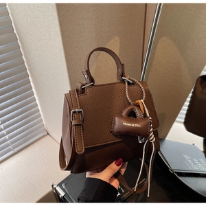 Detail of brown lychee grain leather handbag with top handle and Maven & Chic charm