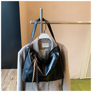 Détail du sac cabas en similicuir noir brillant avec logo embossé et pendentif tissé