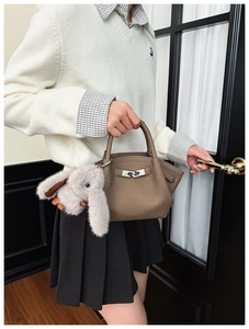 Detail of brown lychee grain bucket bag with silver lock and grey plush rabbit charm